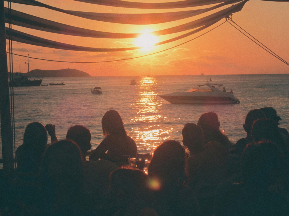 People on a sunset terrace watching the sun drop into the sea.